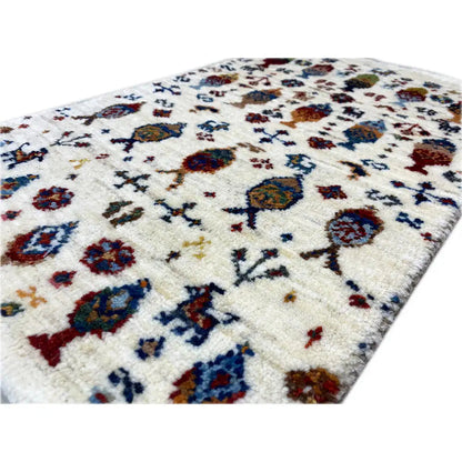 Gabbeh rug close-up: cream-colored pile with colorful figures and ornaments.