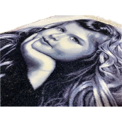 Close-up: tapestry with a portrait of a girl and fringe along the edge.
