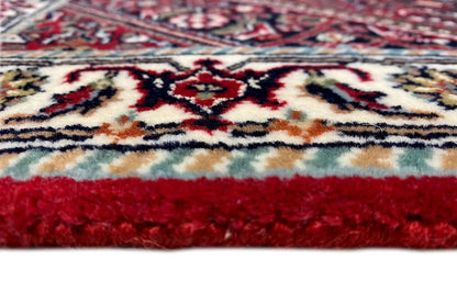 Close-up of carpet edge: red pile, multicolored patterned border, and short fringes