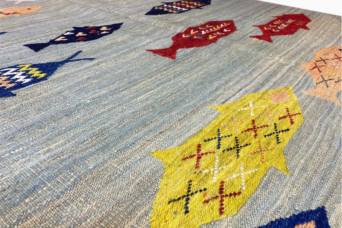 Close-up: yellow fish figure and blue patterns on a light kilim background