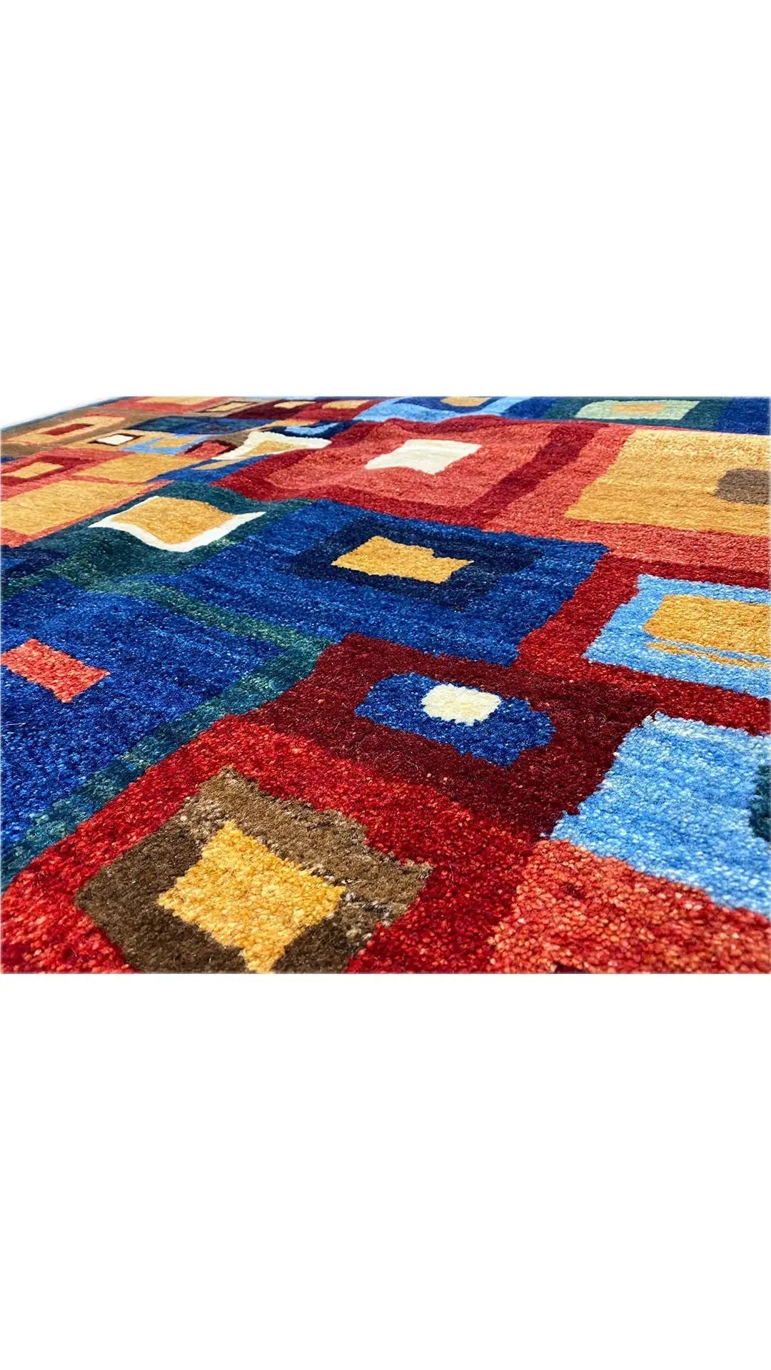 Close-up of a Gabbeh rug, high-contrast blocks in blue, red, beige, and yellow.
