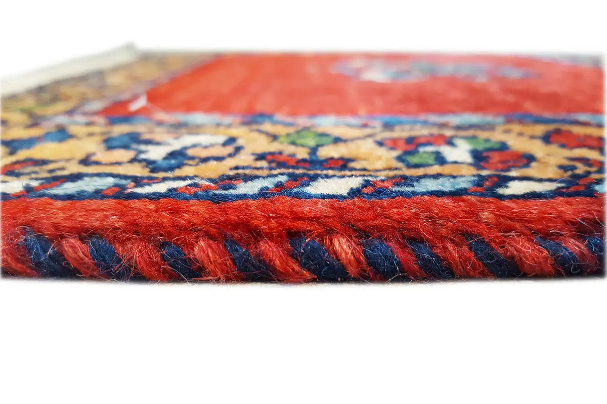 Side view of a red carpet with a blue multicolored border and fringe