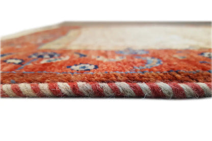 Close-up of a carpet edge: red-and-beige ornamental pattern, with rolled-up pile and fringes.