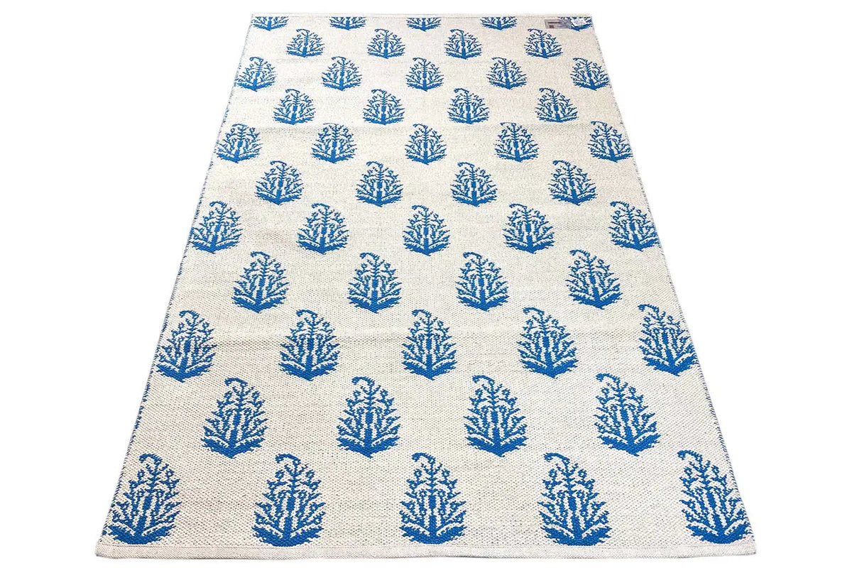 Cream-colored kilim rug with blue tree/branch motifs, an even grid.