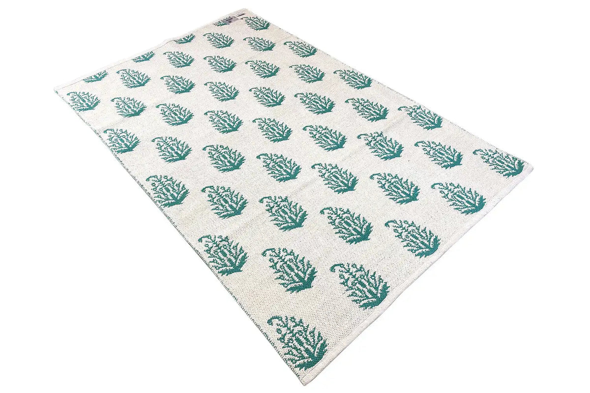 Modern kilim rug with a beige background and green tree pattern, photographed at an angle