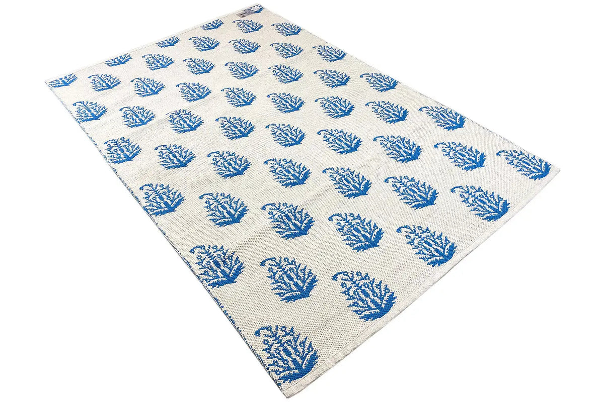 Cream-colored kilim with blue tree/branch motifs, rectangular, arranged diagonally.