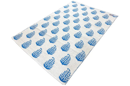 Cream-colored kilim with blue tree/branch motifs, compact weave structure and edges.