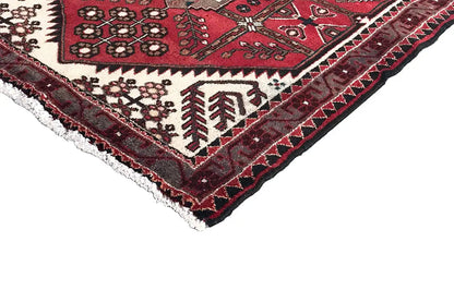 Corner detail of the Hamadan rug: red fabric with floral ornaments and fringes