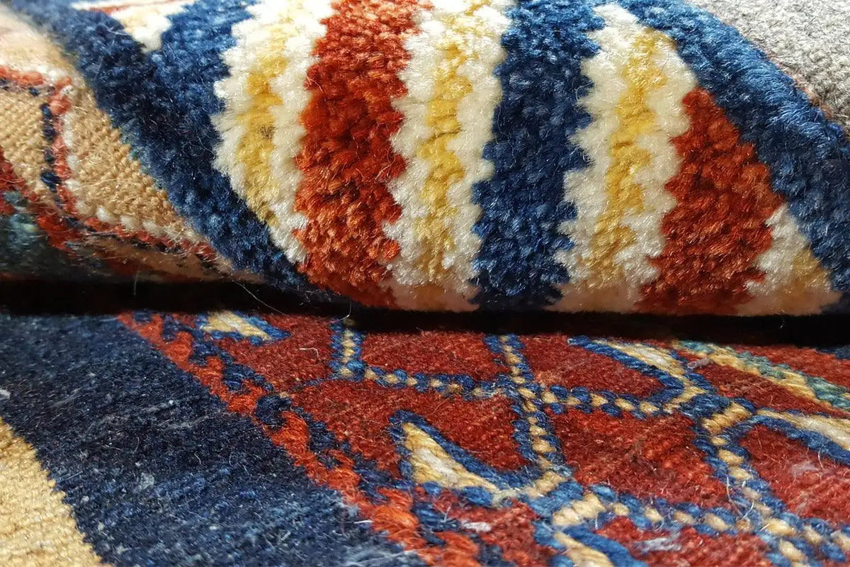 Close-up of a kilim rug: blue, red, and cream-colored patterned stripes, woven fringe