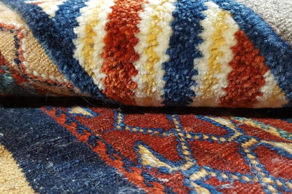 Close-up of a kilim rug: blue, red, and cream-colored patterned stripes, woven fringe