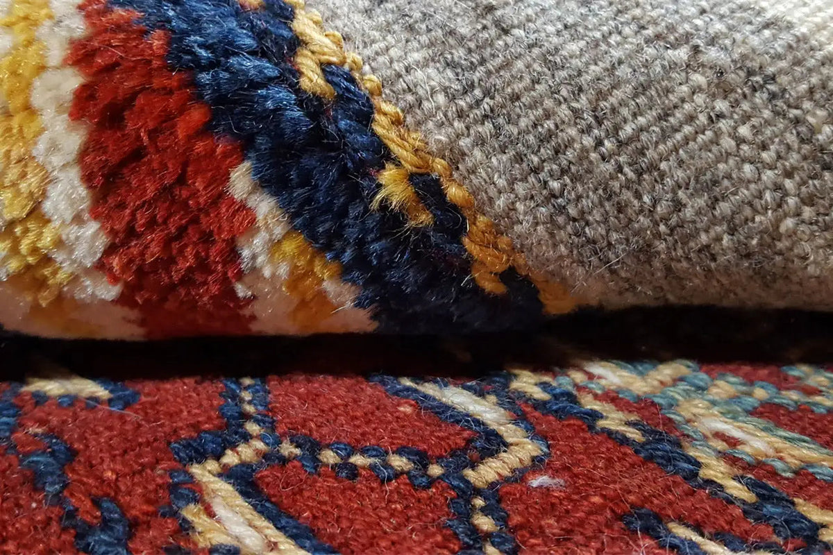 Close-up of a kilim rug: colored stripes, a mottled woven texture, and fringe along the edge.
