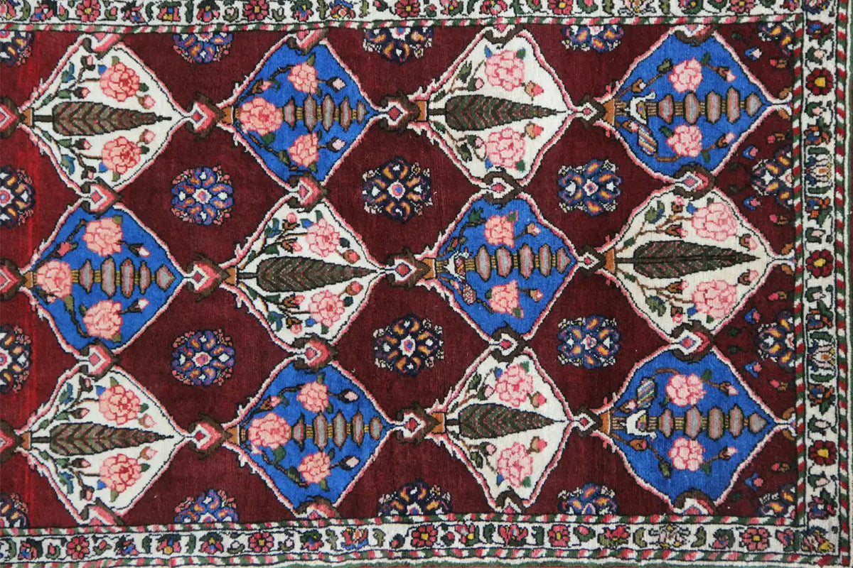 Bakhtiari rug: burgundy background with geometric motifs in blue, cream, and beige.