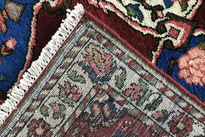 Corner of a Bakhtiari rug with fringes and a dense weave; multicolored patterns on a burgundy background.
