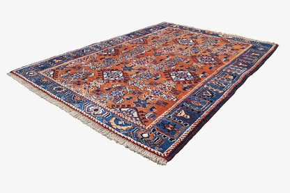 Rug viewed from an angled perspective with an orange-blue pattern and short fringes