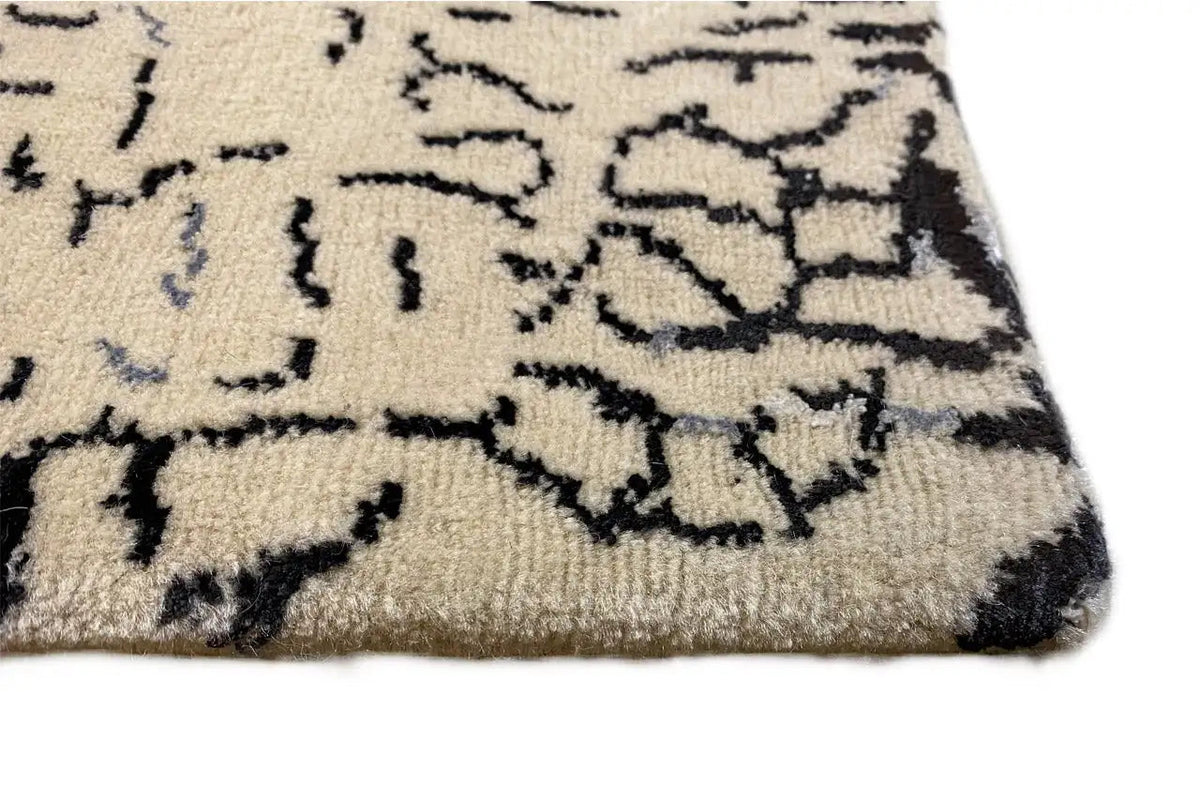 Designer rug: geometric blue-black design on beige pile, corner view