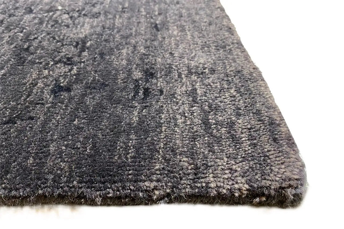 Rug corner with a dark, textured pile surface in blue-gray