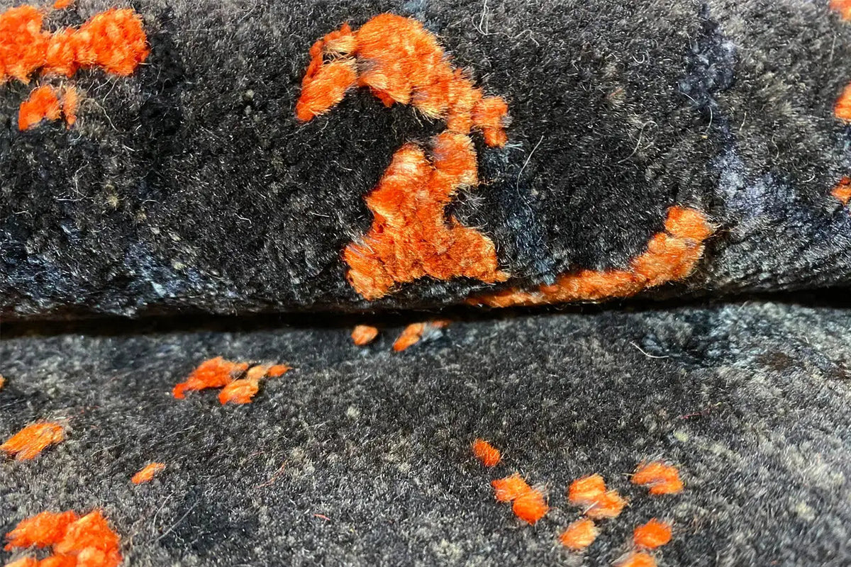 Carpet detail: dark blue-gray with abstract orange speckles and patches of color