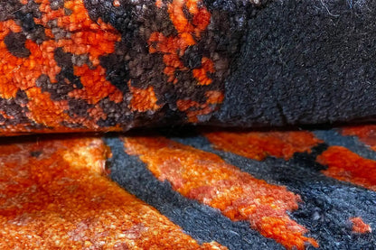 Carpet detail: anthracite-colored surface with orange ornaments and a fringed edge.