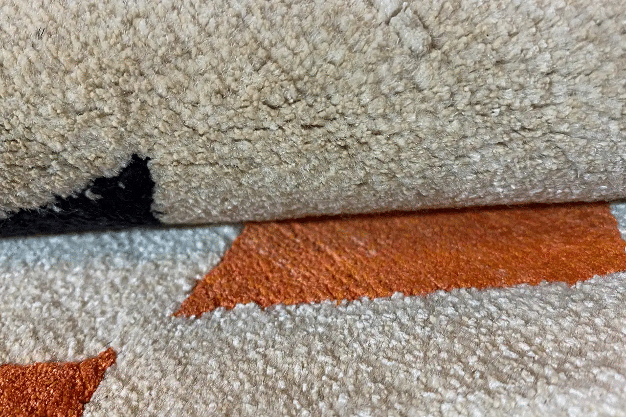 Carpet edge with light beige pile and orange line pattern, close-up.