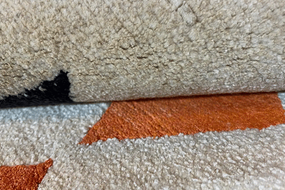 Carpet edge with light beige pile and orange line pattern, close-up.