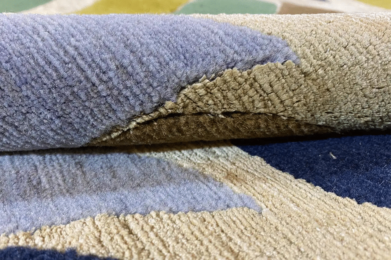 Carpet edge with rolled pile; wave pattern in blue, beige, and cream (close-up)
