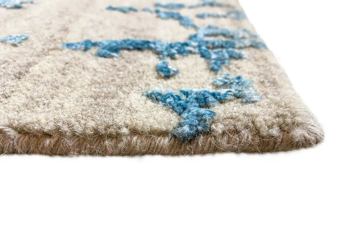 Beige-based carpet pile with a blue pattern, visible wool texture along the edge