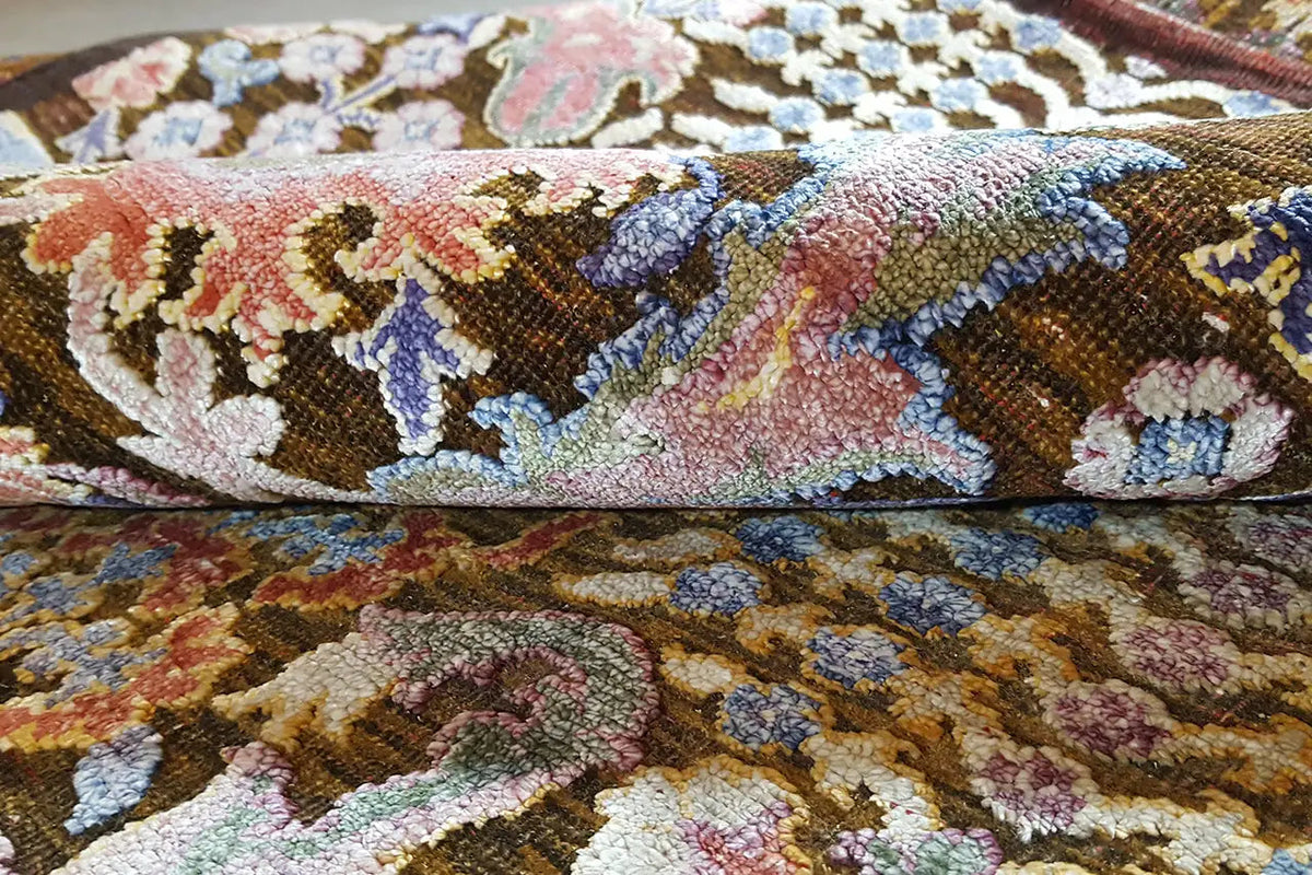 Carpet detail with a relief-like pile and colorful ornamental motif on a dark brown background.