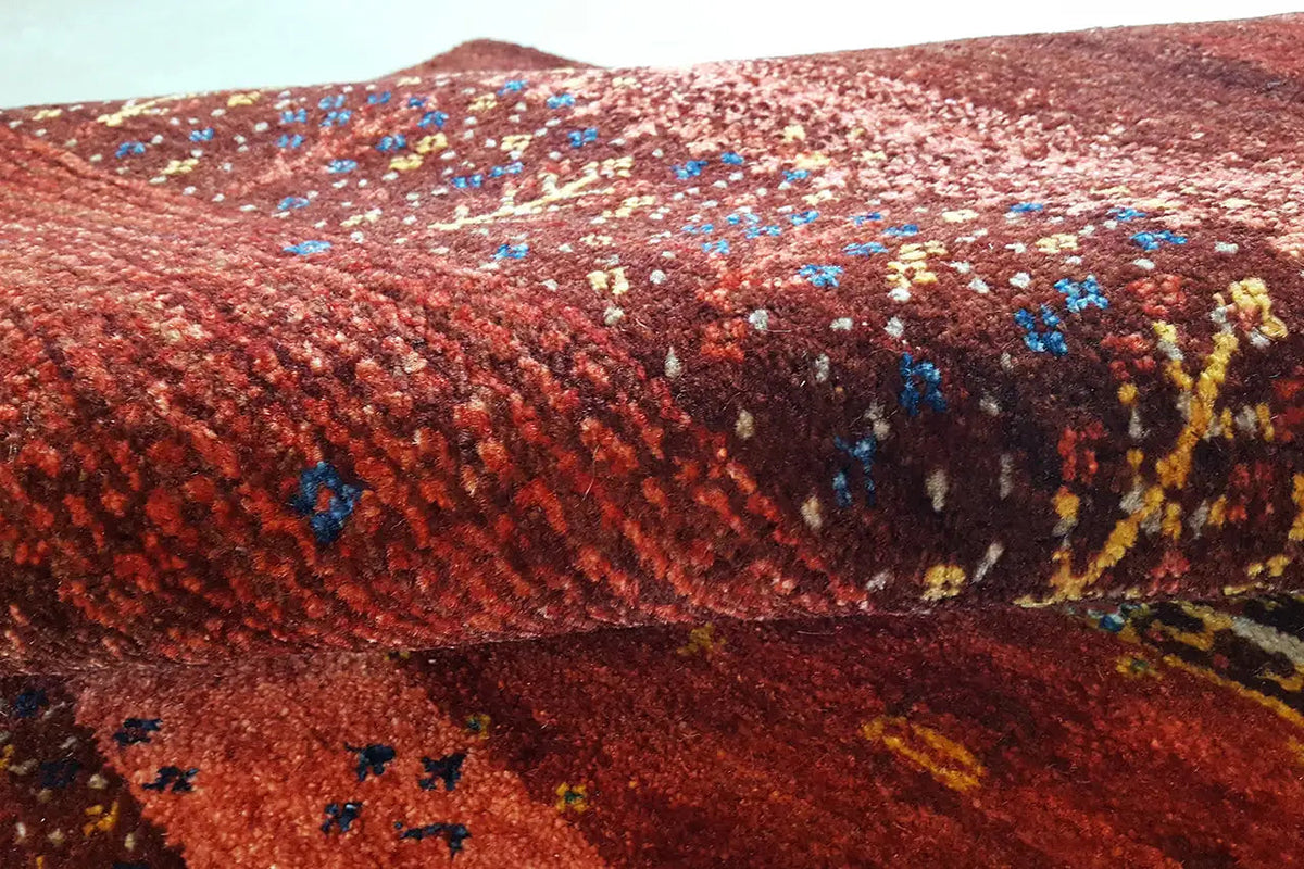 Gabbeh rug with a reddish pile surface and colorful patterned dots in detail.