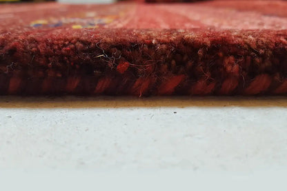 Gabbeh rug edge view: reddish pile with a dense texture and fine color threads.