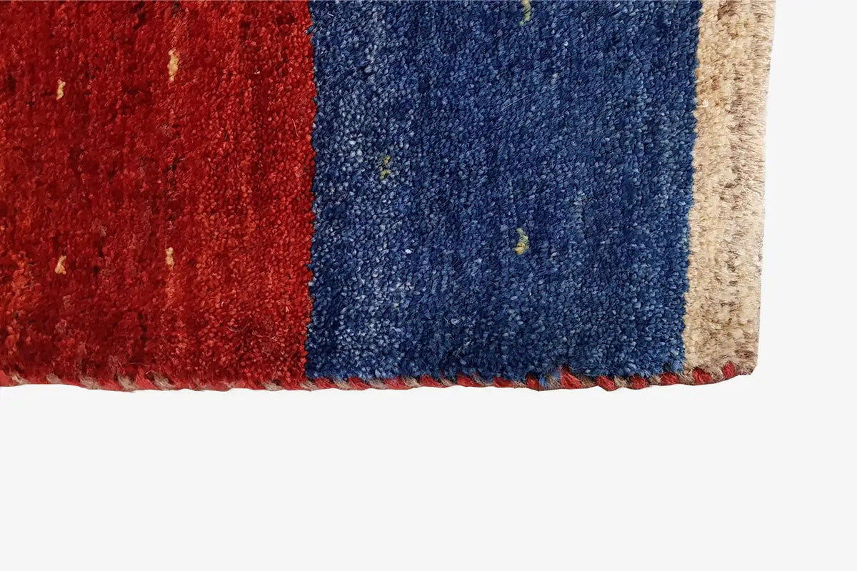 Gabbeh rug corner with red and blue pile and a beige border, rectangular.