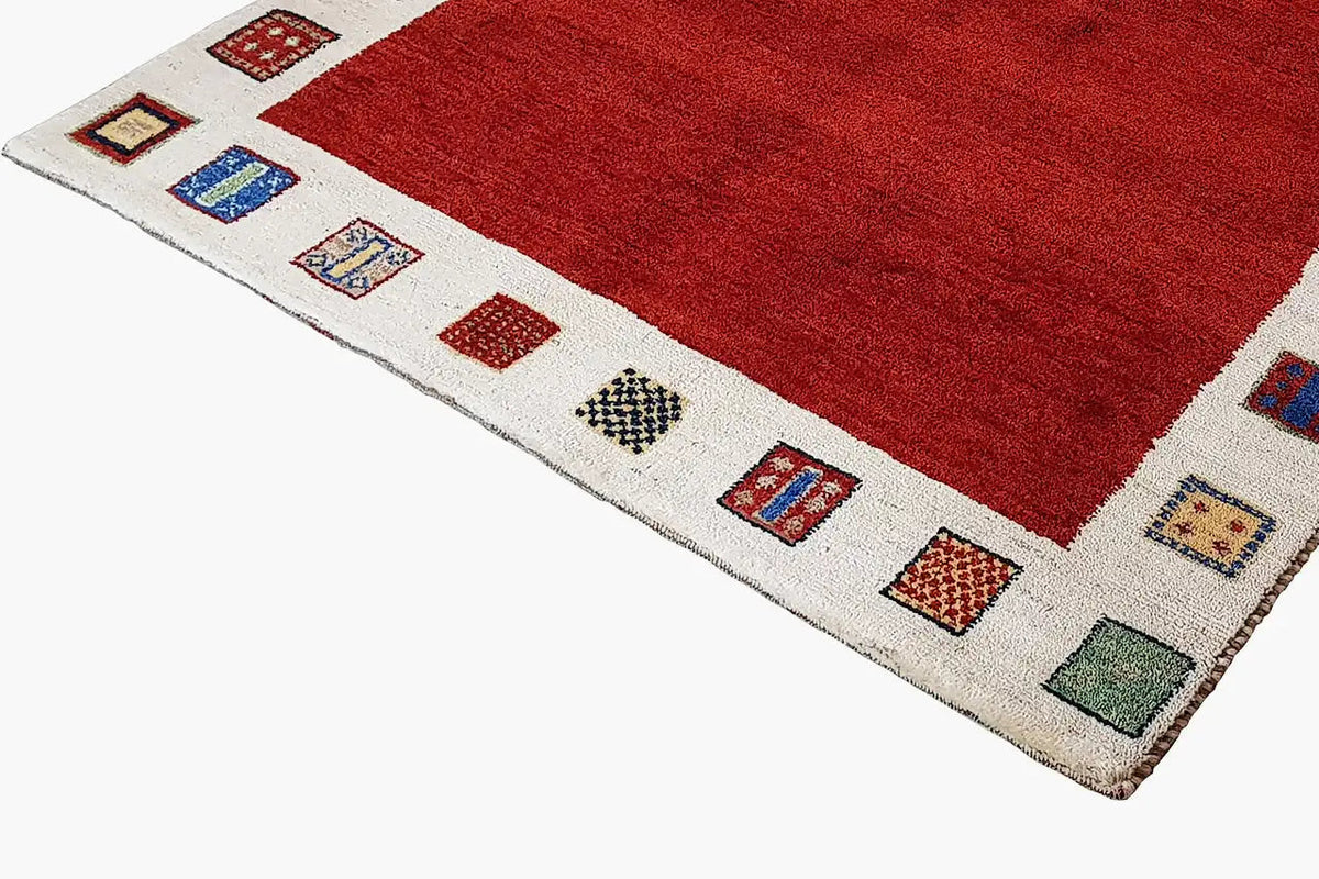 Gabbeh rug: red pile, beige border with colorful square patterns, close-up of the corner