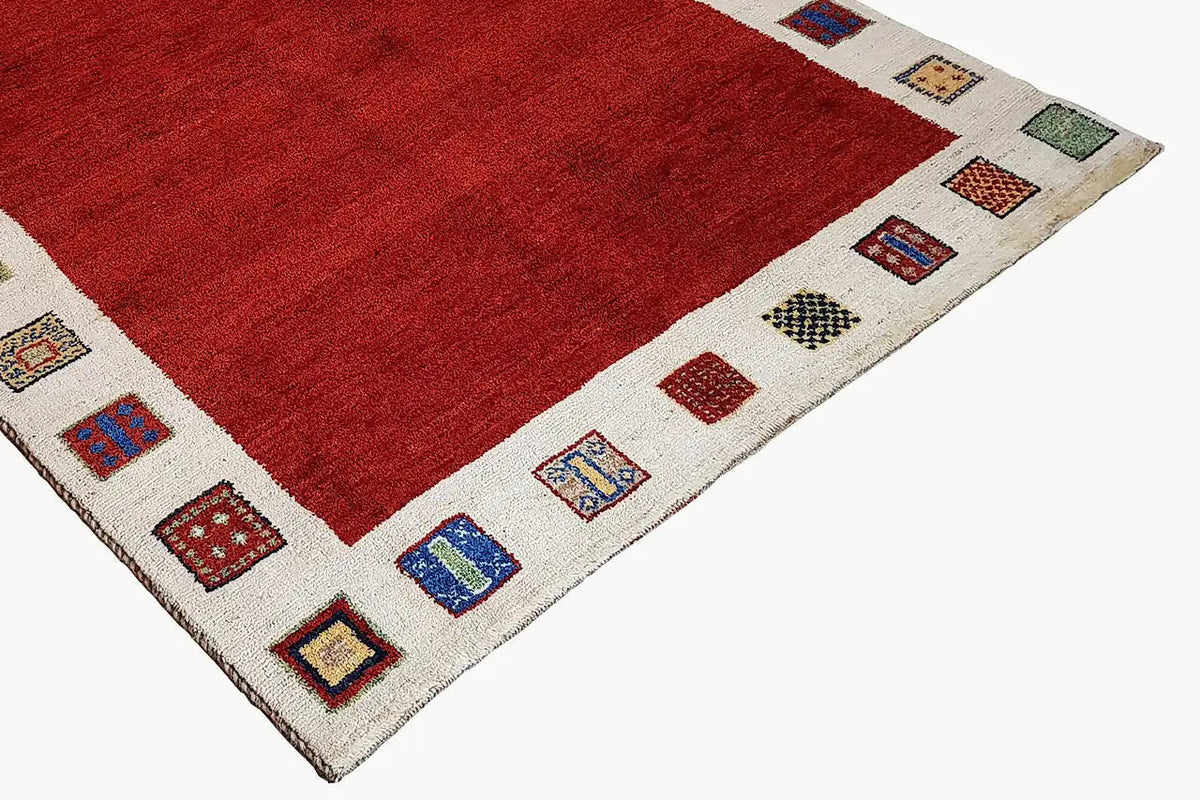 Gabbeh rug corner: red pile area and beige border with colorful decorative squares