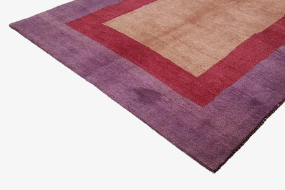 Close-up of Gabbeh rug: purple pile with a red square border and beige center.