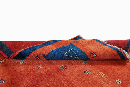 Red Gabbeh rug with a blue border and colorful geometric patterns, with fringes