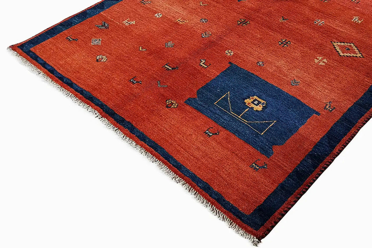 Red rectangular rug with a blue corner motif, colorful symbols, and fringes