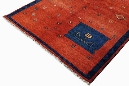 Red rectangular rug with a blue corner motif, colorful symbols, and fringes