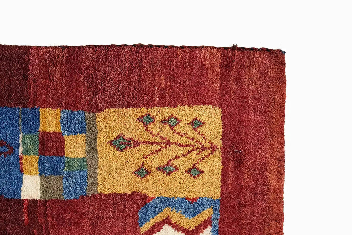 Gabbeh rug corner with a red pile, multicolored squares, and a visible border finish