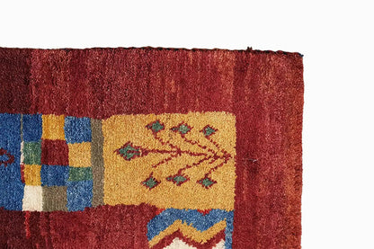 Gabbeh rug corner with a red pile, multicolored squares, and a visible border finish