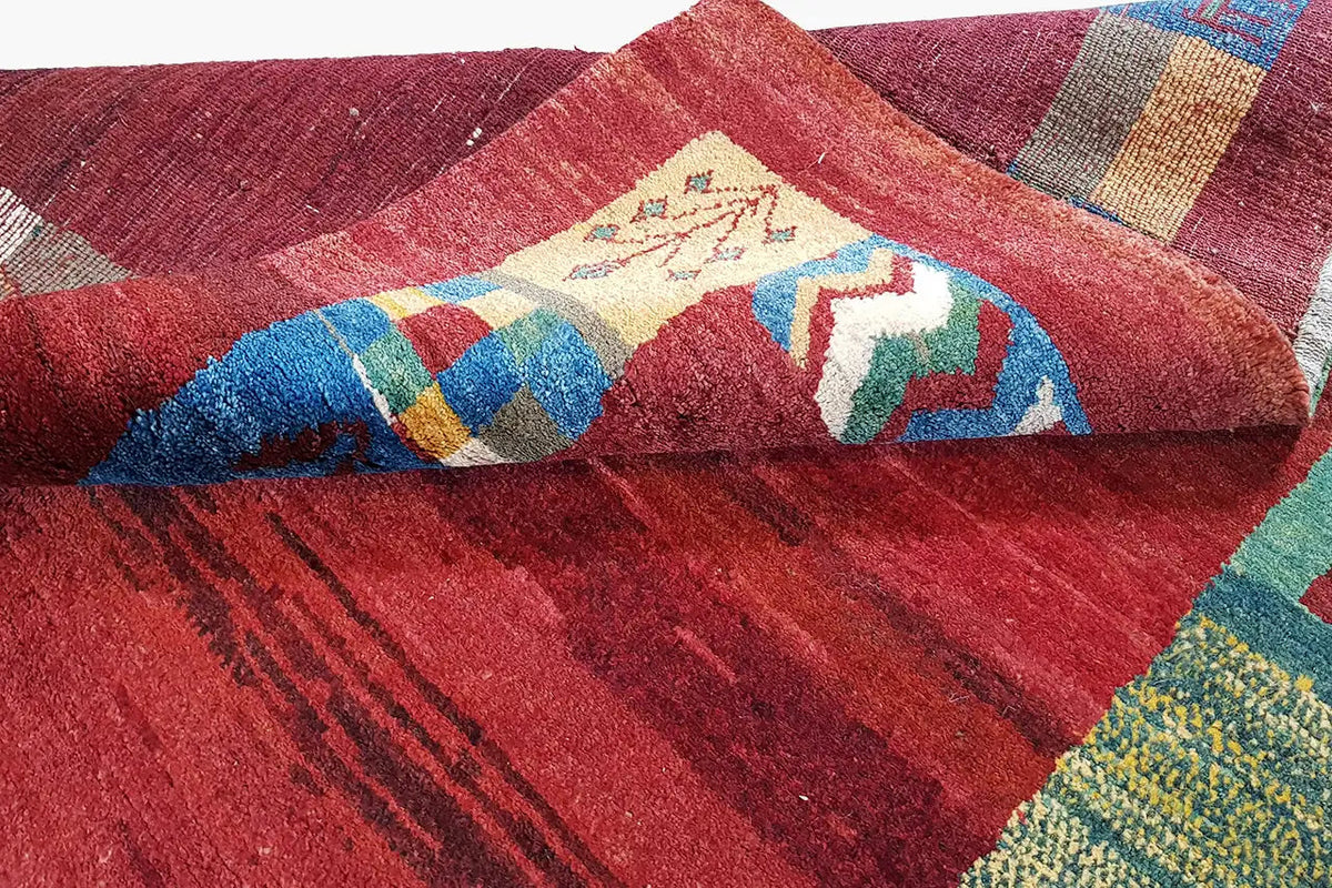 Gabbeh rug detail with a red surface and patchwork of blue, green, and yellow areas