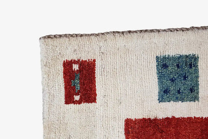 Gabbeh rug corner: cream-colored pile with red and blue square design, bordered