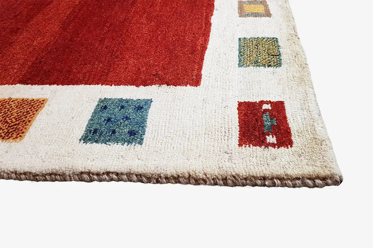 Gabbeh rug edge with colorful square motifs on a cream-colored background and short fringes