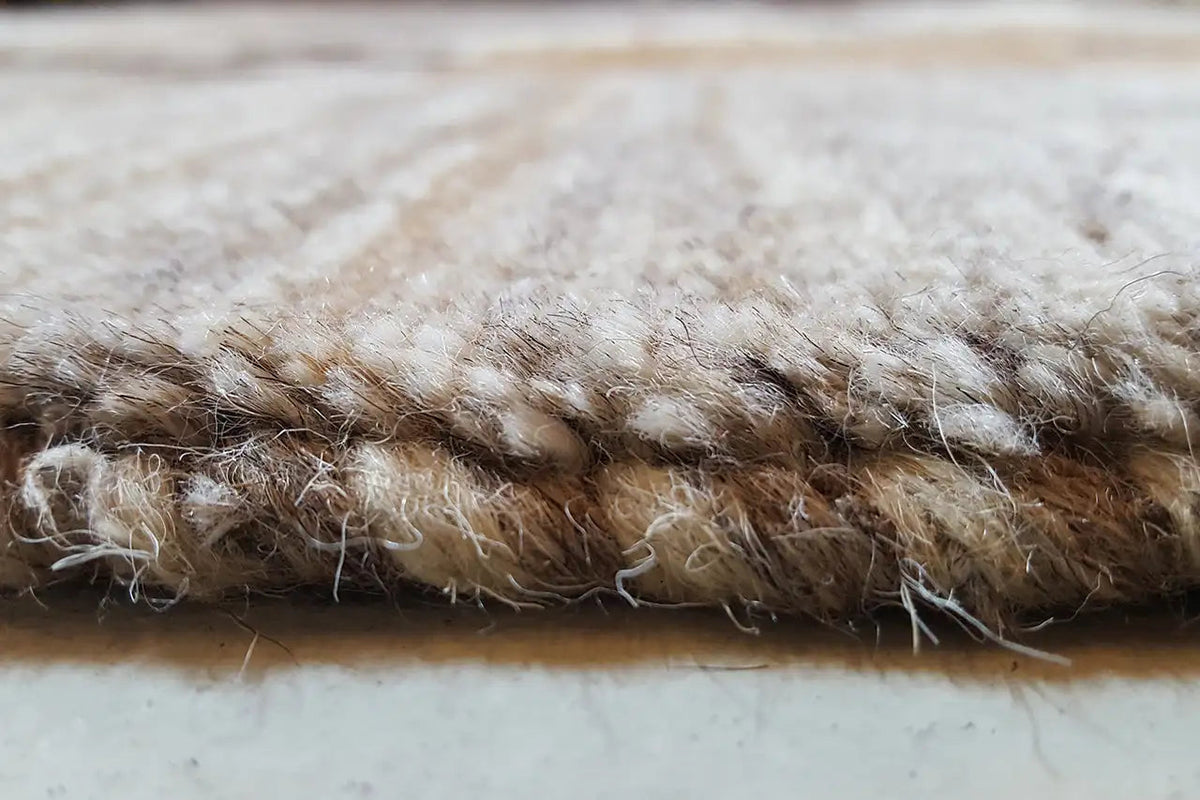 Rug edge with dense pile, brown-beige threads, and a slightly frayed edge