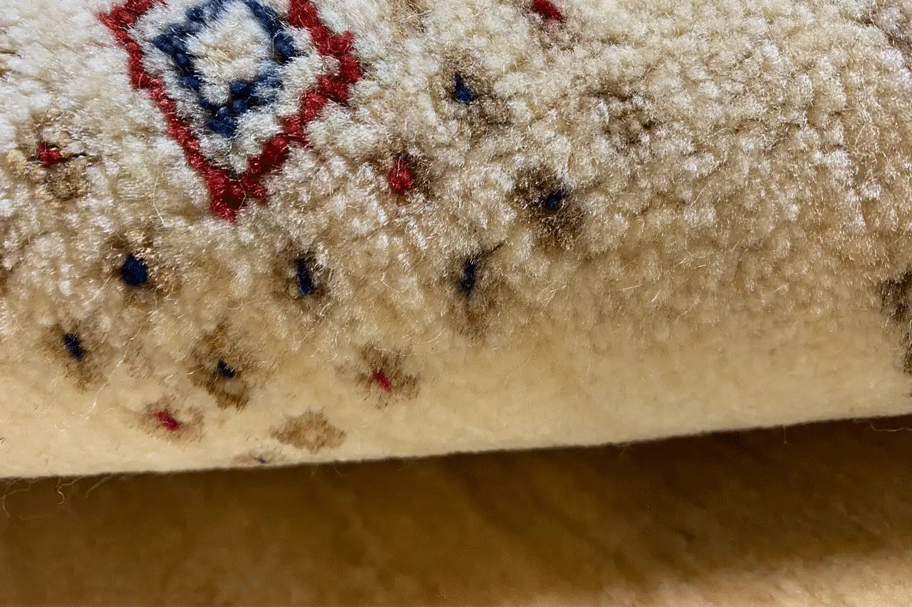 Close-up of a carpet edge with a wool pile and colorful square motif in dark blue