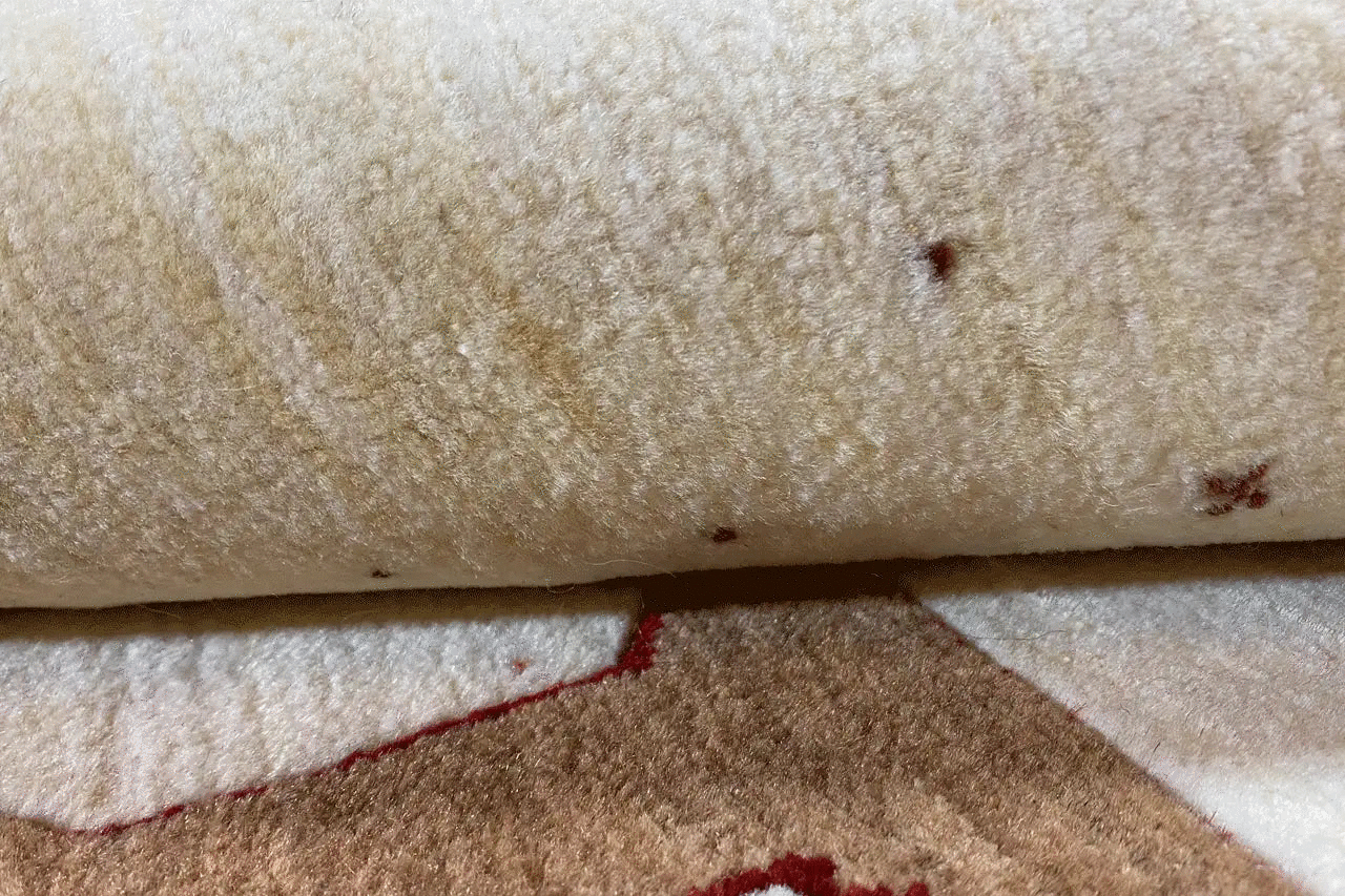Gabbeh rug detail: light wool texture with reddish-brown patches and fine speckles