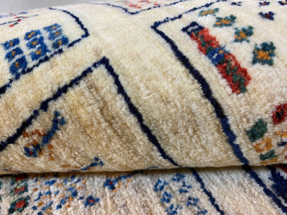 Gabbeh rug close-up: beige pile with a blue contour pattern and colorful accents
