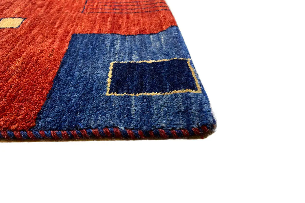 Close-up detail of the Gabbeh rug: red-and-blue pattern, short fringes along the edge