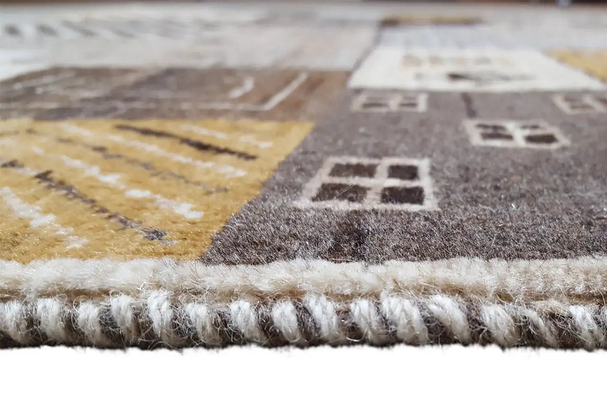 Gabbeh rug edge with fringes and beige pile, gray-brown shading along the edge.
