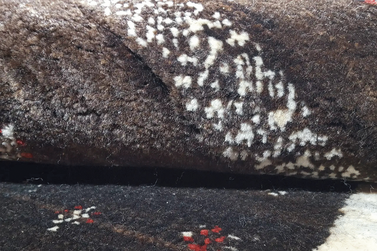 Detail of the Gabbeh rug: dark pile surface with a contrasting white pattern and subtle color accents.