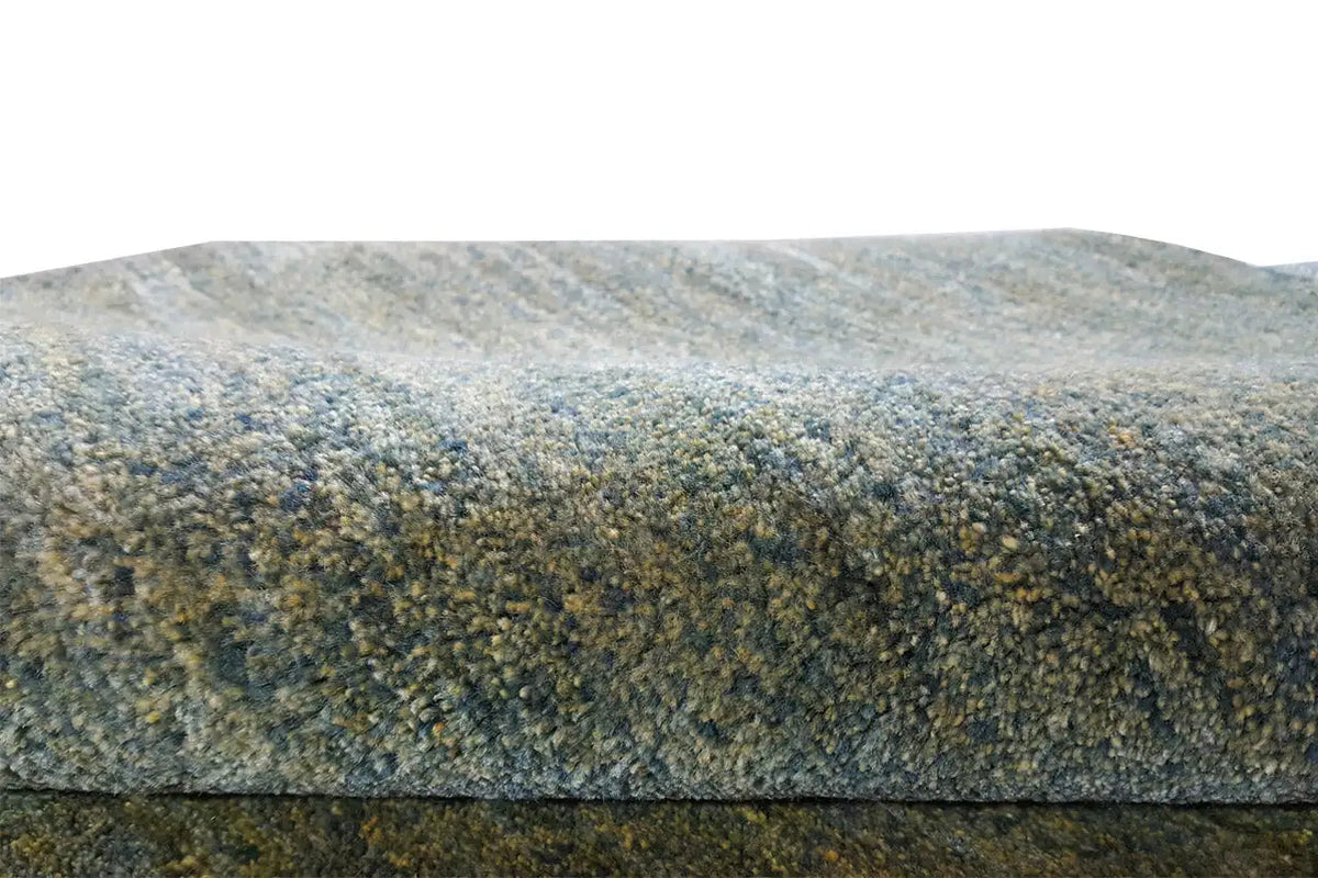 Gabbeh rug with green-gray pile texture and visible edge, mottled