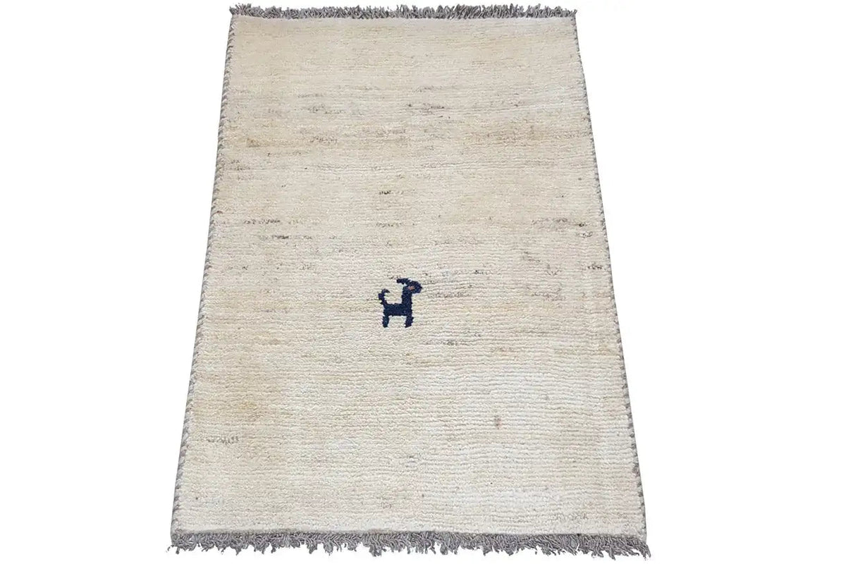 Cream-colored Gabbeh rug, dark fringes, blue H-shaped decorative motif in the center